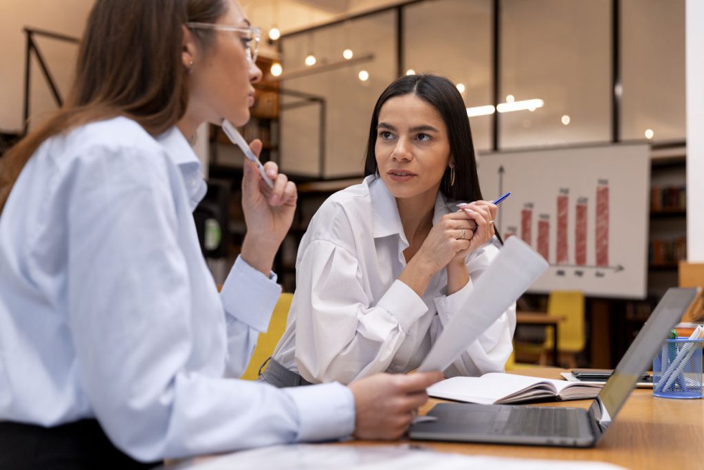 Imagem mostra duas mulheres de negócios conversando, com gráficos atrás delas, para simular como abrir empresa de bpo financeiro