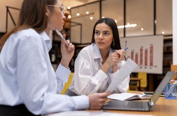 Imagem mostra duas mulheres de negócios conversando, com gráficos atrás delas, para simular como abrir empresa de bpo financeiro