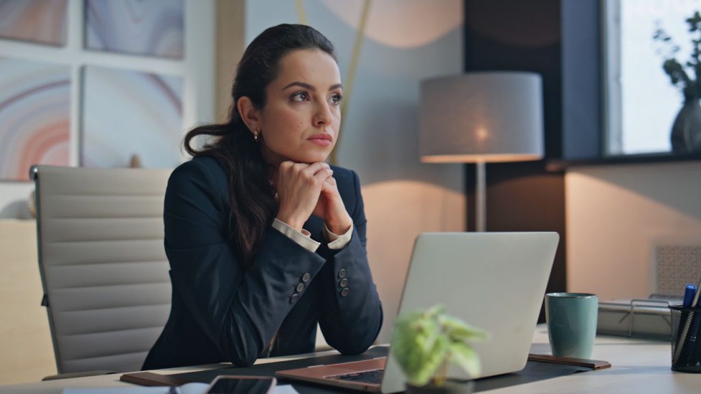 Jovem empresária sentada à mesa de seu escritório, pensativa, como se avaliasse se franquia de contabilidade vale a pena