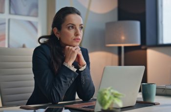 Jovem empresária sentada à mesa de seu escritório, pensativa, como se avaliasse se franquia de contabilidade vale a pena