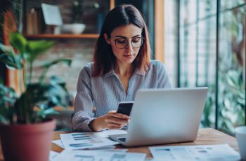 Imagem mostra mulher mexendo no computador com papéis em sua mesa, para ilustrar como abrir um escritório de contabilidade online