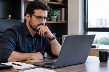 Imagem mostra contador em seu escritório olhando reflexivo para o notebook, como se analisasse a plataforma Sieg